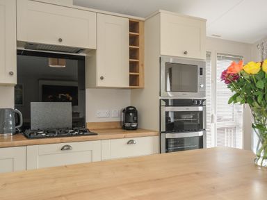 A kitchen with a gas stove kettle coffee maker built in microwave and oven and a vase with flowers on a wooden table at Lodge 59 at Riviera Bay Coastal Retreat Brixham