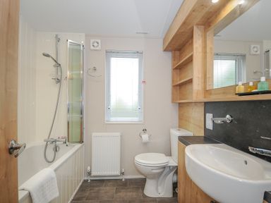A bathroom with a bathtub shower combination a toilet a sink and wood cabinets with mirror at Lodge 59 at Riviera Bay Coastal Retreat in Brixham
