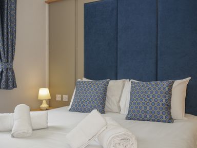 A bedroom with a bed with blue patterned cushions white towels and a bedside lamp at Lodge 59 at Riviera Bay Coastal Retreat in Brixham