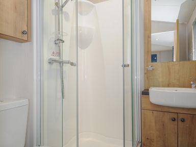 A bathroom with a glass shower enclosure a sink with wooden cabinet a mirror and a toilet at Lodge 59 at Riviera Bay Coastal Retreat in Brixham