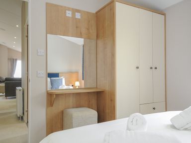 A bedroom with a built-in wardrobe dressing table and a bed with towels at Lodge 59 at Riviera Bay Coastal Retreat in Brixham