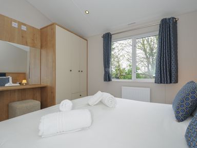 A bedroom with a bed towels wardrobe mirror and window with curtains at Lodge 59 at Riviera Bay Coastal Retreat Brixham