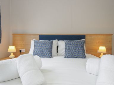 A bed with white bedding and patterned blue cushions with rolled white towels on the bed at Lodge 59 at Riviera Bay Coastal Retreat in Brixham