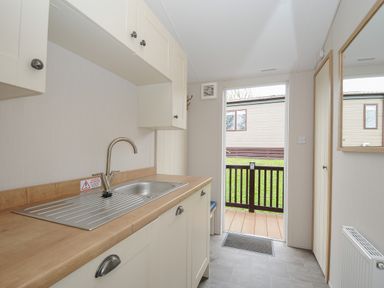 A kitchen area with a sink and cabinets next to an open door showing an outside deck at Lodge 59 at Riviera Bay Coastal Retreat in Brixham