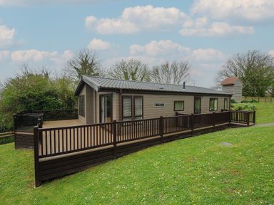 A single-story cabin with a wooden deck and fenced yard on a grassy hill at Lodge 59 at Riviera Bay Coastal Retreat in Brixham