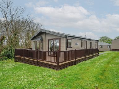 A single story cabin with a fenced deck surrounded by grass and trees at Lodge 63 at Riviera Bay Coastal Retreat in Brixham