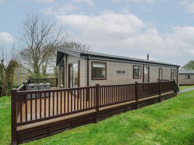 An exterior view of a detached lodge with a wooden deck and railing on a grassy area at Lodge 63 at Riviera Bay Coastal Retreat Brixham