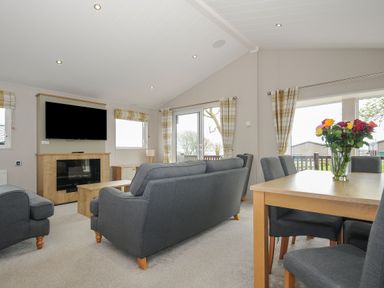 A living room with grey sofas a wooden dining table and a TV mounted above a fireplace at Lodge 69 at Riviera Bay Coastal Retreat in Brixham