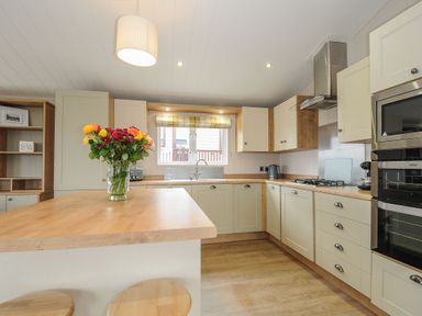 A kitchen with a wooden countertop island with flowers on it and built in appliances at Lodge 69 at Riviera Bay Coastal Retreat in Brixham