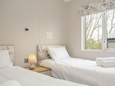 A bedroom with two single beds a bedside table with a lamp and a window with trees outside at Lodge 69 at Riviera Bay Coastal Retreat Brixham