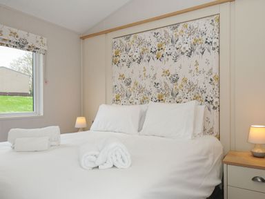 A bedroom with a bed with white linens towels a wooden bedside table and lamp at Lodge 69 at Riviera Bay Coastal Retreat in Brixham