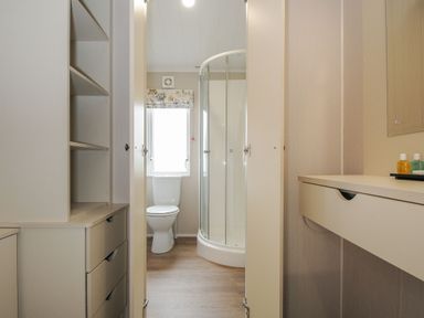 A bathroom with a toilet and a corner shower visible through an open door with cabinets and a drawer on the sides at Lodge 69 at Riviera Bay Coastal Retreat in Brixham