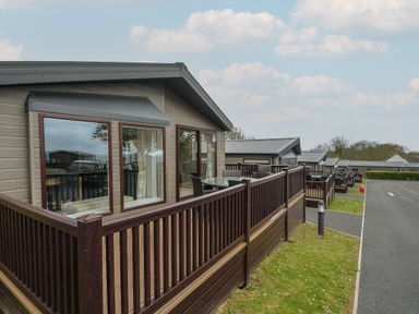 A row of lodges with wooden decks and outdoor tables next to a paved road at Lodge 68 at Riviera Bay Coastal Retreat in Brixham