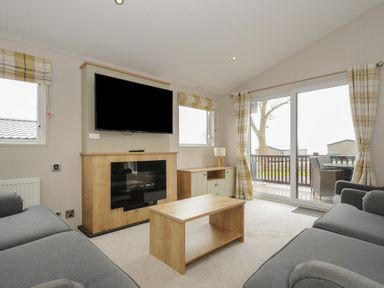 A living room with two grey sofas a wooden coffee table a wall mounted television and sliding glass doors at Lodge 68 at Riviera Bay Coastal Retreat in Brixham