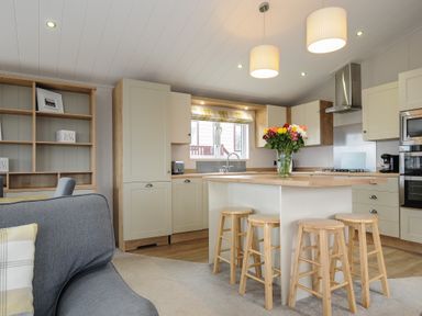 A kitchen with wooden stools around an island and flowers on the counter at Lodge 68 at Riviera Bay Coastal Retreat in Brixham