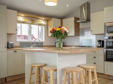 A kitchen with wooden stools around an island and a vase of flowers on the counter at Lodge 68 at Riviera Bay Coastal Retreat in Brixham