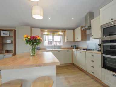 A kitchen with wooden countertops a vase of flowers on the island and built in ovens at Lodge 68 at Riviera Bay Coastal Retreat in Brixham