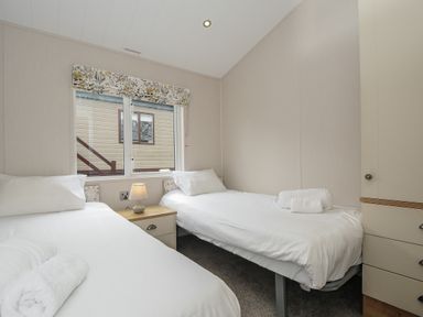 A bedroom with two single beds a window a nightstand with a lamp and a wardrobe at Lodge 68 at Riviera Bay Coastal Retreat in Brixham