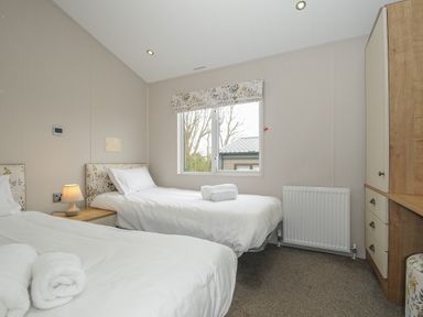 A bedroom with two single beds a window and a wooden wardrobe with drawers at Lodge 68 at Riviera Bay Coastal Retreat in Brixham