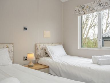 A bedroom with two single beds a wooden nightstand with a lamp and a window showing trees outside at Lodge 68 at Riviera Bay Coastal Retreat Brixham