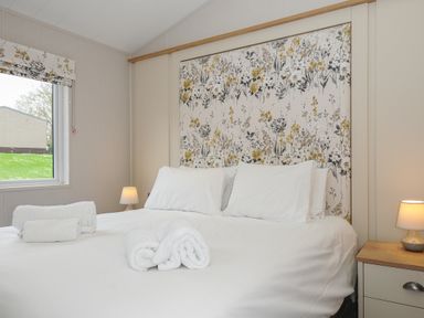 A bedroom with a double bed with white linens and floral headboard at Lodge 68 at Riviera Bay Coastal Retreat in Brixham