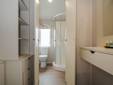 A bathroom with a toilet and a shower with glass doors seen from a doorway at Lodge 68 at Riviera Bay Coastal Retreat in Brixham