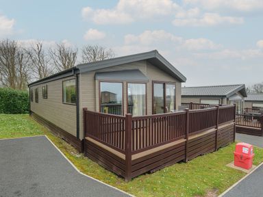A wooden cabin with a fenced deck and surrounding grassy area at Lodge 70 at Riviera Bay Coastal Retreat in Brixham
