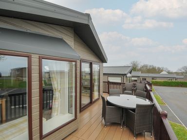 A balcony with a round glass table and six chairs outside a wooden cabin at Lodge 70 at Riviera Bay Coastal Retreat in Brixham