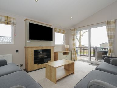 A living room with two gray sofas a wooden coffee table a wall-mounted TV and glass doors leading to a balcony at Lodge 70 at Riviera Bay Coastal Retreat in Brixham
