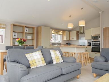 An open living room and kitchen with gray sofas and yellow plaid pillows at Lodge 70 at Riviera Bay Coastal Retreat in Brixham