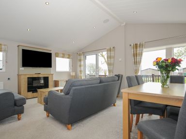 A living room with gray sofas a wooden dining table with chairs and flowers on it at Lodge 70 at Riviera Bay Coastal Retreat in Brixham