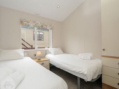 A bedroom with two single beds a bedside table with a lamp and a window at Lodge 70 at Riviera Bay Coastal Retreat in Brixham