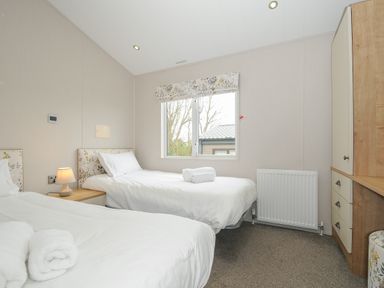 A bedroom with two single beds bedside lamp window and wardrobe at Lodge 70 at Riviera Bay Coastal Retreat in Brixham