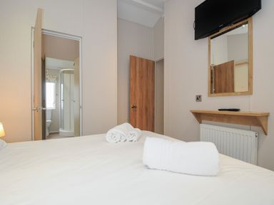 A bedroom with a bed towels a wall-mounted TV a mirror and an open door showing a bathroom at Lodge 70 at Riviera Bay Coastal Retreat in Brixham