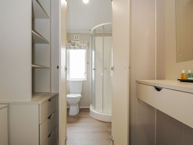 A bathroom with a toilet a corner shower unit and storage cabinets at Lodge 70 at Riviera Bay Coastal Retreat in Brixham