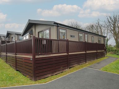 An exterior view of a mobile home with wooden railing and paved pathway at Lodge 70 at Riviera Bay Coastal Retreat in Brixham