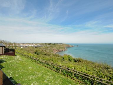 A coastal landscape with grassy area and wooden fence overlooking cliffs and the sea at Chalet 7 at Landscove Holiday Park in Brixham