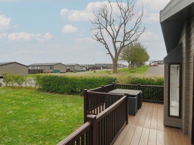 A wooden deck with table and chairs overlooking grass and trees at Lodge 73 at Riviera Bay Coastal Retreat in Brixham