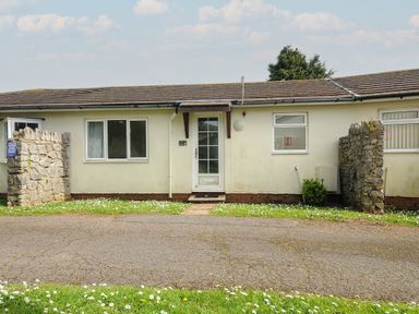 A single-story building with a white door and windows with stone pillars on each side at Chalet 27 at Landscove Holiday Park in Brixham