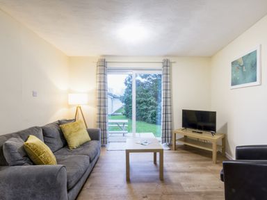 A living room with a sofa, television, and sliding door at Chalet 27 at Landscove Holiday Park Brixham