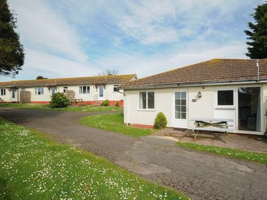 Bungalow houses with picnic tables on lawn and paved pathway under blue sky at Chalet 31 at Landscove Holiday Park in Brixham
