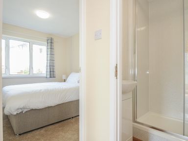A bedroom with a bed and window next to a bathroom with a shower and sink at Chalet 31 at Landscove Holiday Park in Brixham
