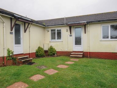 A grassy yard with stepping stones leading to two doors on a single-story building at Chalet 15 at Landscove Holiday Park in Brixham