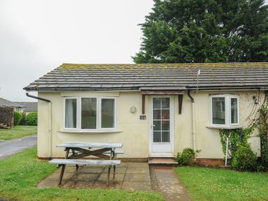 A bungalow with a picnic table on a paved area in front at Chalet 33 at Landscove Holiday Park in Brixham