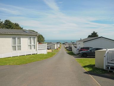 A road lined with holiday chalets and parked cars overlooking the sea at Chalet 34 at Landscove Holiday Park in Brixham