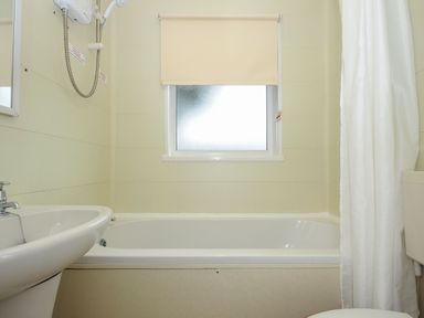 A bathroom with a bathtub sink shower curtain and window with blind at Chalet 34 at Landscove Holiday Park Brixham