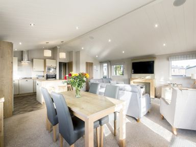 An open plan living area with a dining table and kitchen units at Lodge 9 at Landscove Holiday Park Brixham