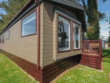 An exterior view of a beige and brown mobile home with large windows and a wooden deck at Lodge 11 at Landscove Holiday Park in Brixham