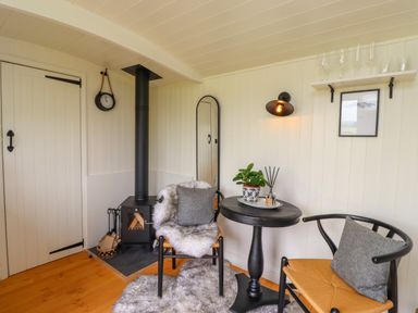 A small room with a wood stove two chairs a round table and a wall shelf at La'al Ling in Penrith