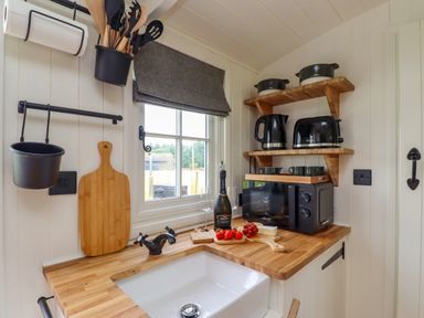 A kitchen corner with a wooden countertop sink cutting boards a microwave kettle toaster cups and cooking utensils at La'al Ling in Penrith